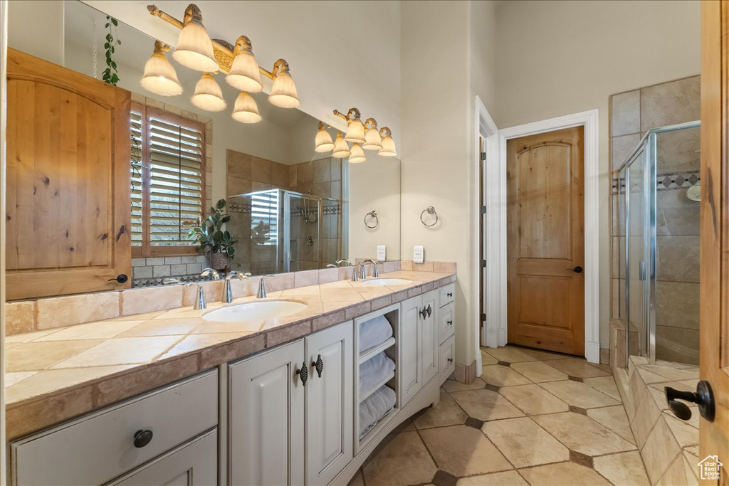 Bathroom featuring an enclosed shower, double sink, vanity with extensive cabinet space, and tile floors