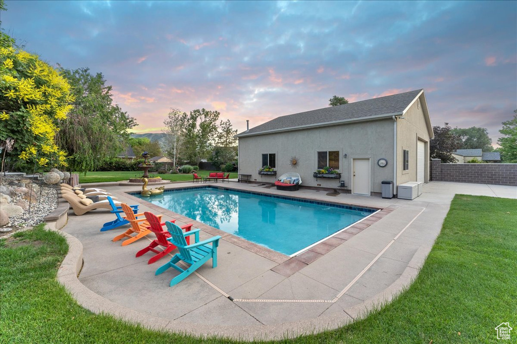 Pool at dusk with a patio and a lawn