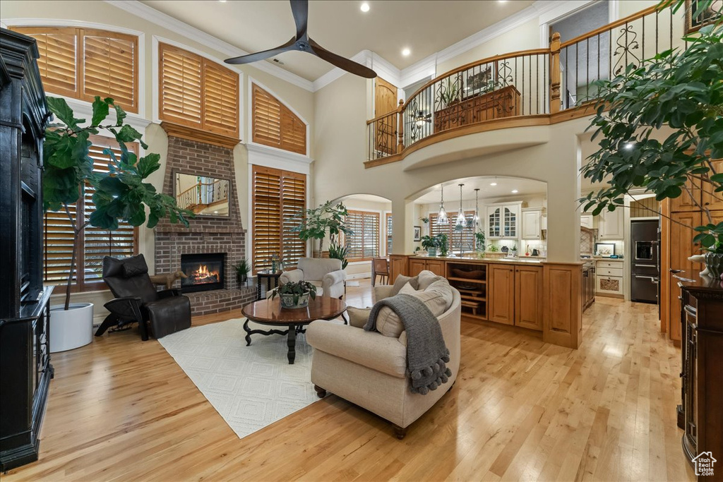 Living room with a brick fireplace, light hardwood / wood-style floors, ornamental molding, beverage cooler, and ceiling fan