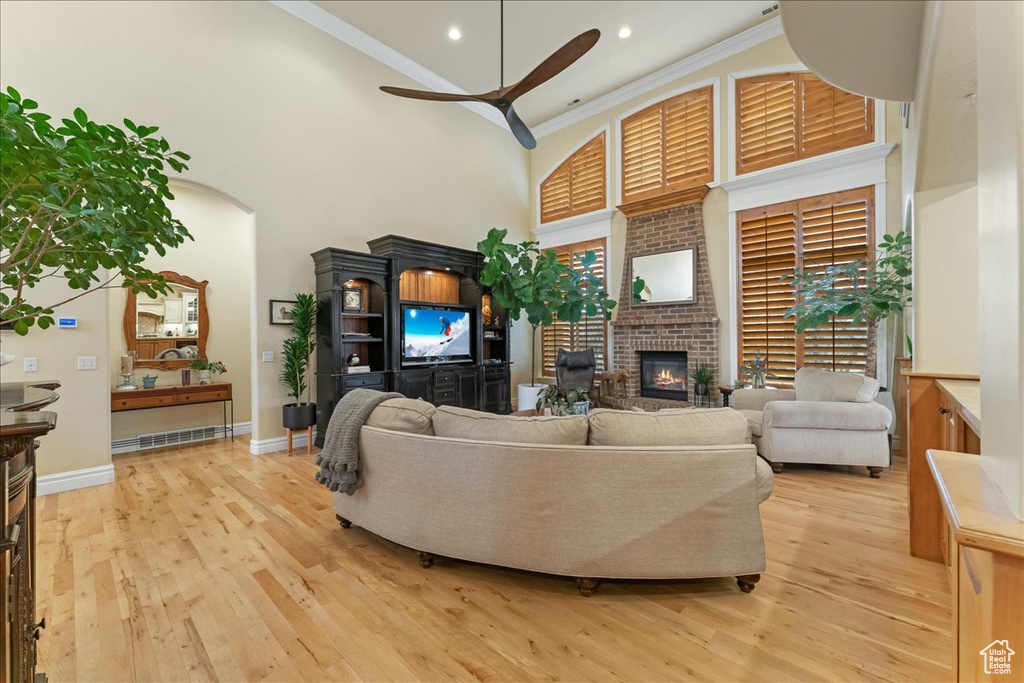Living room with a fireplace, light hardwood / wood-style floors, ornamental molding, a towering ceiling, and ceiling fan