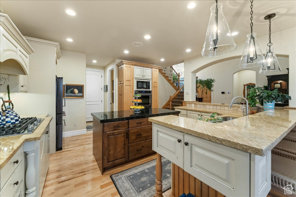 Kitchen featuring black appliances, a kitchen island, light wood-type flooring, and light stone counters