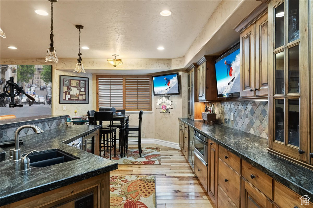 Kitchen with tasteful backsplash, dark stone countertops, sink, light wood-type flooring, and decorative light fixtures