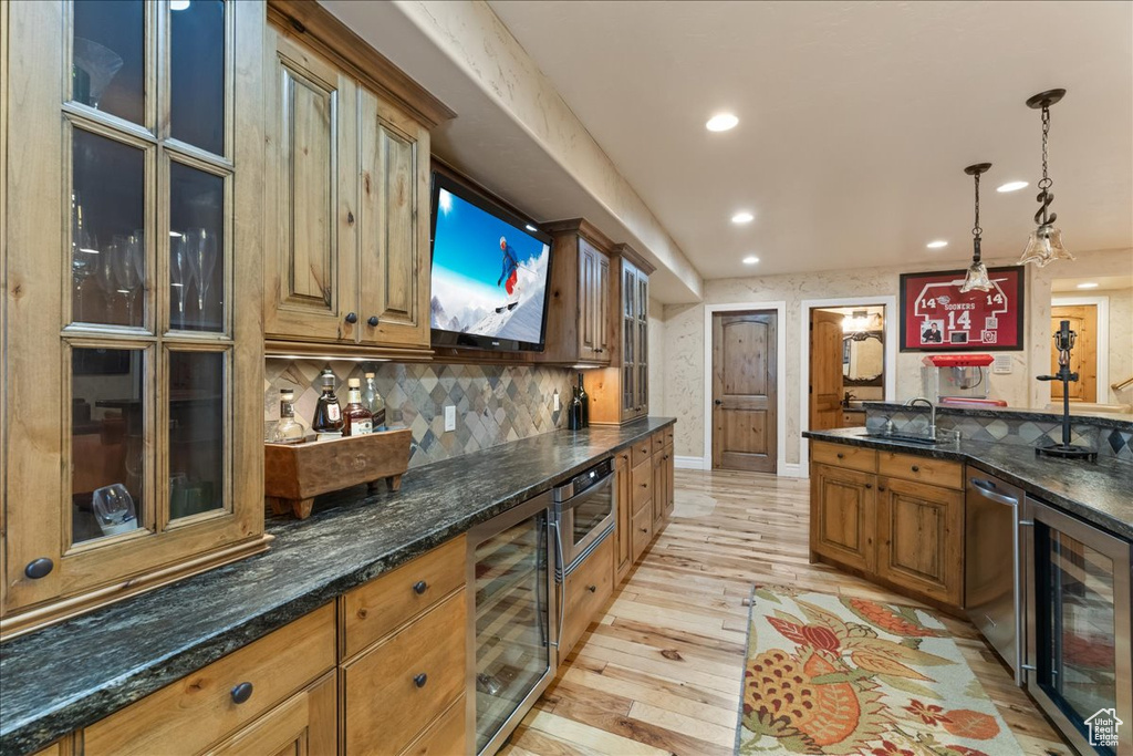 Kitchen featuring dark stone countertops, wine cooler, backsplash, light hardwood / wood-style floors, and hanging light fixtures