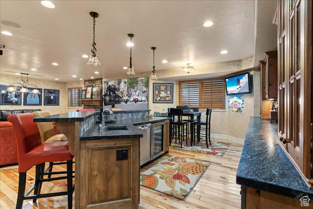 Kitchen featuring hanging light fixtures, an island with sink, light wood-type flooring, and beverage cooler