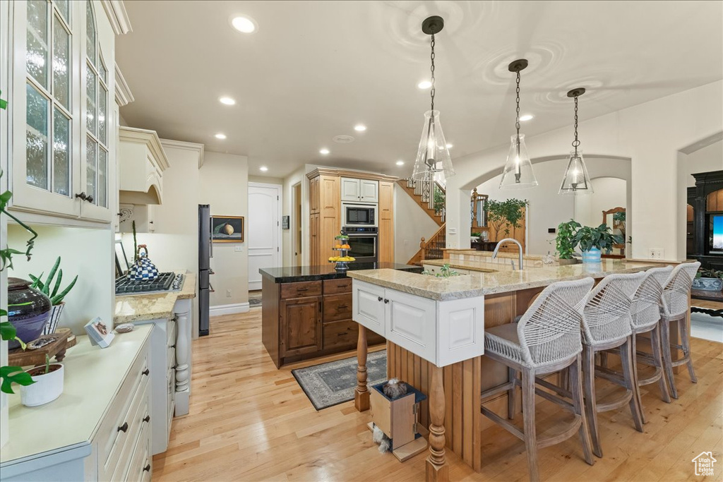 Kitchen with appliances with stainless steel finishes, a center island with sink, light hardwood / wood-style floors, light stone counters, and white cabinetry