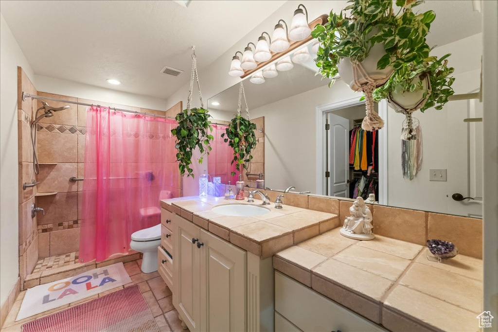 Bathroom with toilet, tile flooring, a shower with shower curtain, and vanity with extensive cabinet space