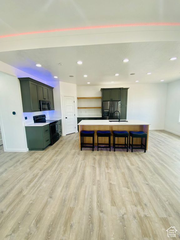 Kitchen with a center island with sink, stainless steel appliances, light hardwood / wood-style floors, and a kitchen bar