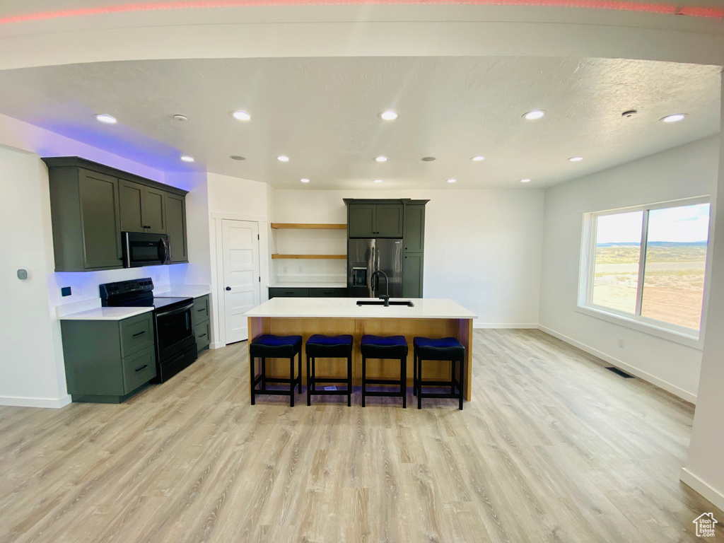 Kitchen with a breakfast bar, sink, light hardwood / wood-style floors, an island with sink, and stainless steel appliances