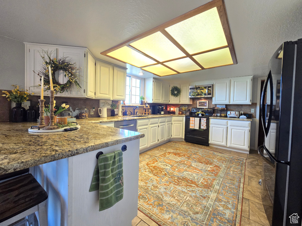 Kitchen featuring backsplash, light tile floors, white cabinetry, and black appliances
