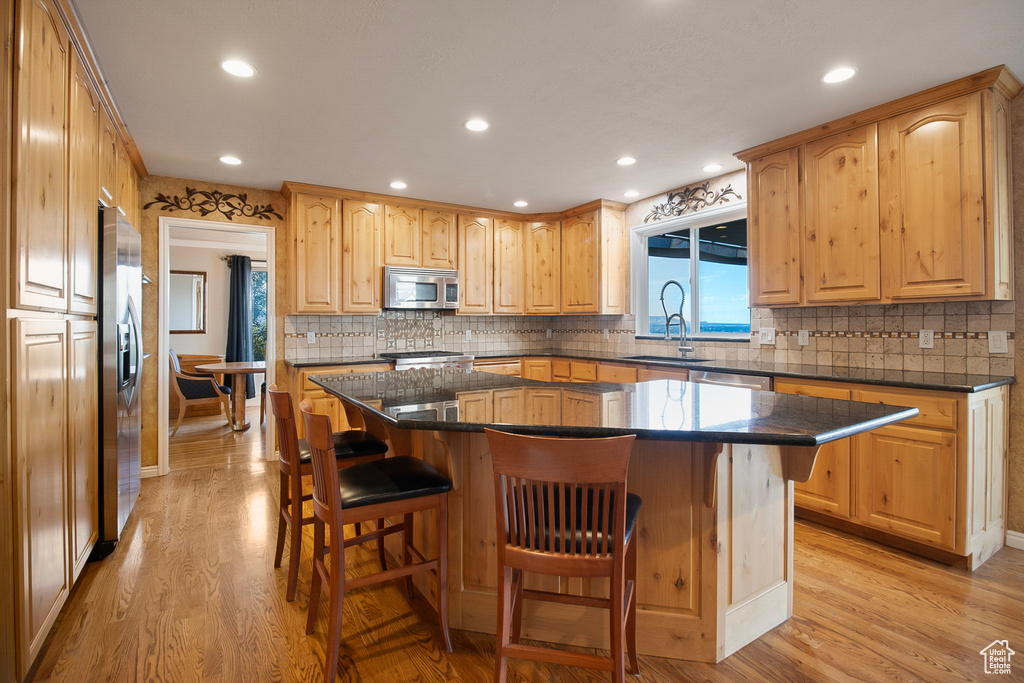 Kitchen with a kitchen island, tasteful backsplash, a kitchen bar, appliances with stainless steel finishes, and light hardwood / wood-style flooring