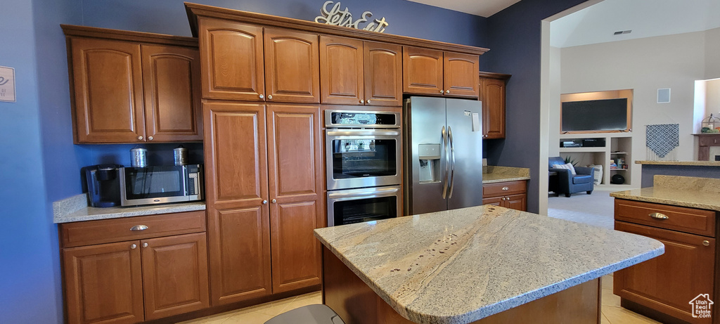 Kitchen featuring appliances with stainless steel finishes, light stone counters, light carpet, and a center island