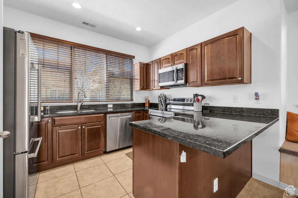 Kitchen featuring appliances with stainless steel finishes, light tile flooring, kitchen peninsula, and dark stone countertops
