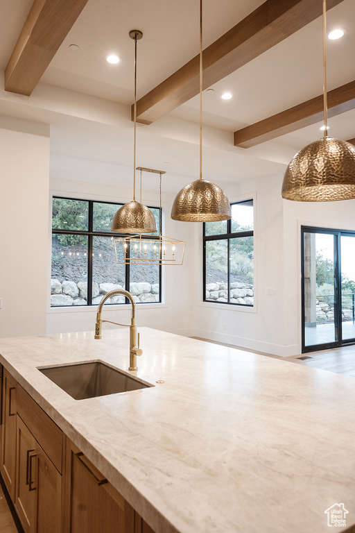 Kitchen with beamed ceiling, sink, light stone countertops, light hardwood / wood-style flooring, and pendant lighting