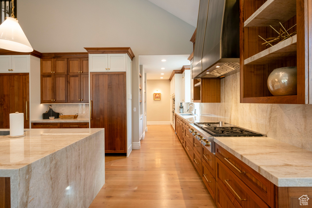 Kitchen featuring wall chimney exhaust hood, light wood-type flooring, backsplash, and decorative light fixtures