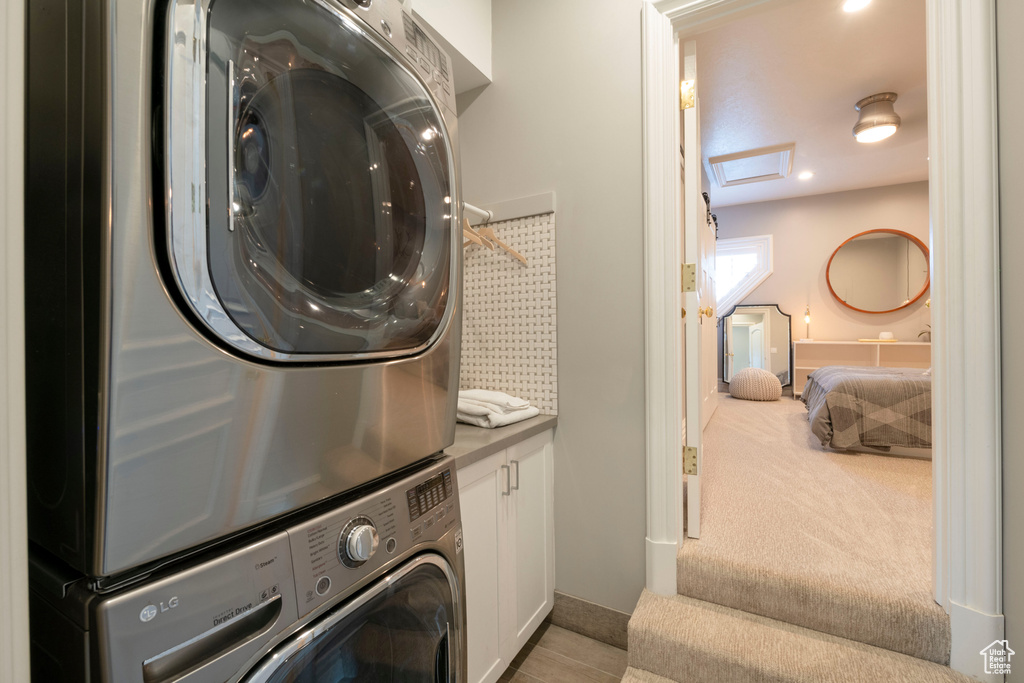 Laundry room with cabinets, light colored carpet, and stacked washer and clothes dryer