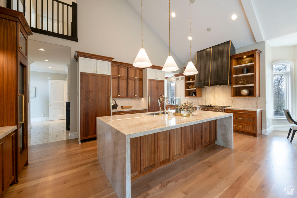 Kitchen with tasteful backsplash, a center island with sink, light stone counters, light hardwood / wood-style flooring, and pendant lighting