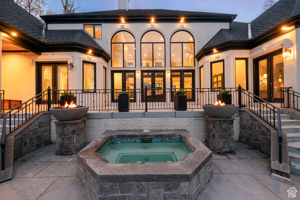 Back house at dusk featuring french doors and an in ground hot tub