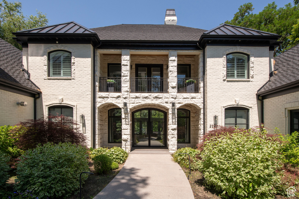 View of front of home featuring french doors, a balcony, a standing seam roof, and brick siding