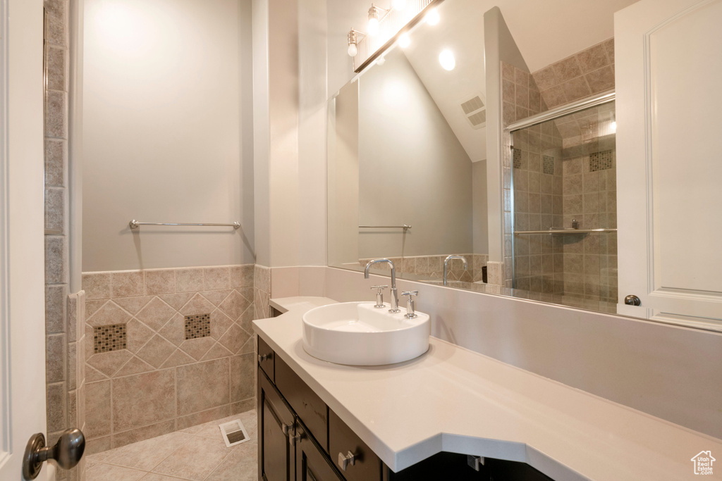 Bathroom featuring tile flooring, vaulted ceiling, oversized vanity, and a shower with door