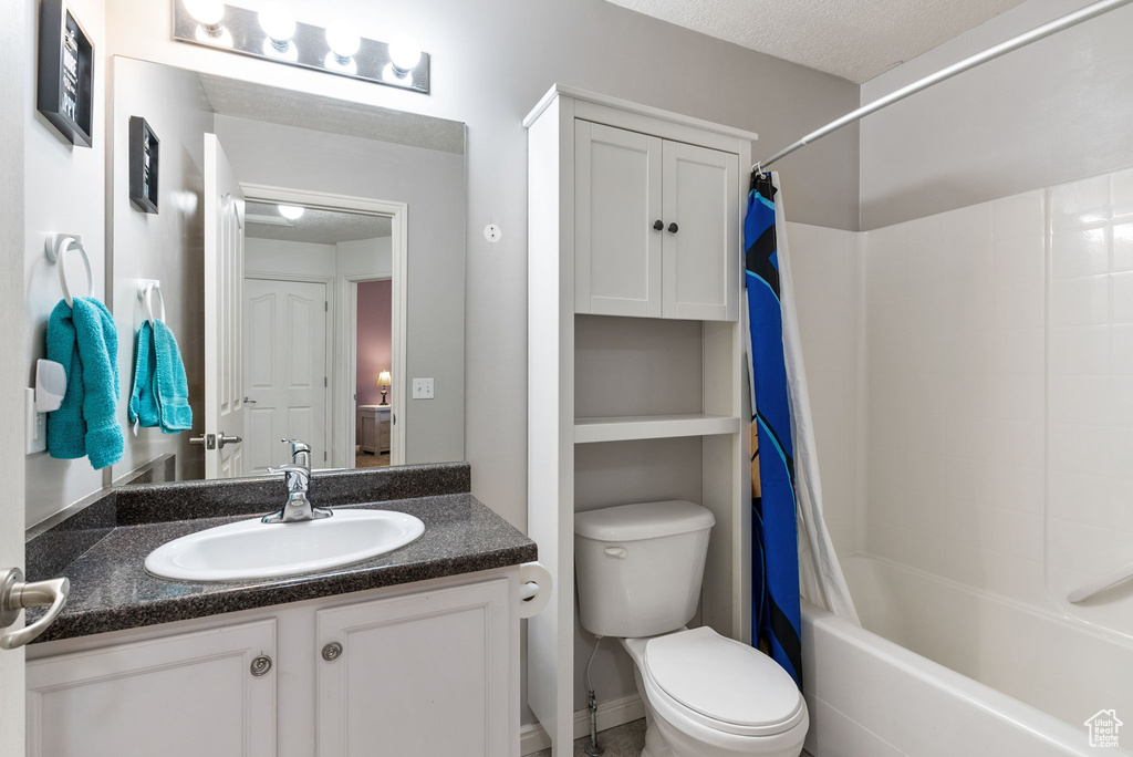 Full bathroom with toilet, shower / bathtub combination with curtain, a textured ceiling, and vanity