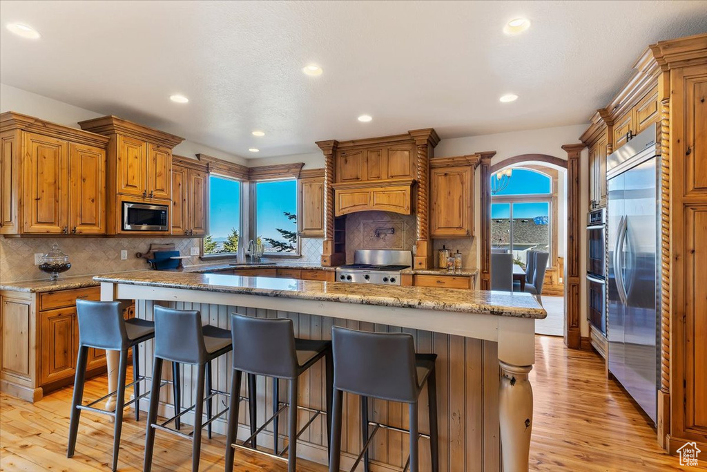Kitchen with light hardwood / wood-style flooring, a center island, backsplash, built in appliances, and a breakfast bar area