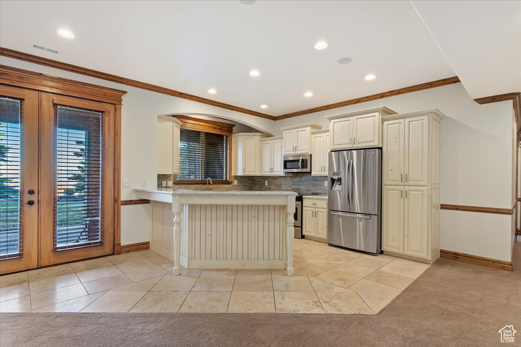 Kitchen with tasteful backsplash, french doors, light colored carpet, appliances with stainless steel finishes, and a breakfast bar area