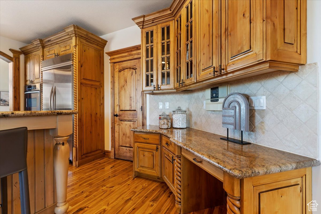Kitchen featuring backsplash, light stone counters, stainless steel oven, and light hardwood / wood-style floors