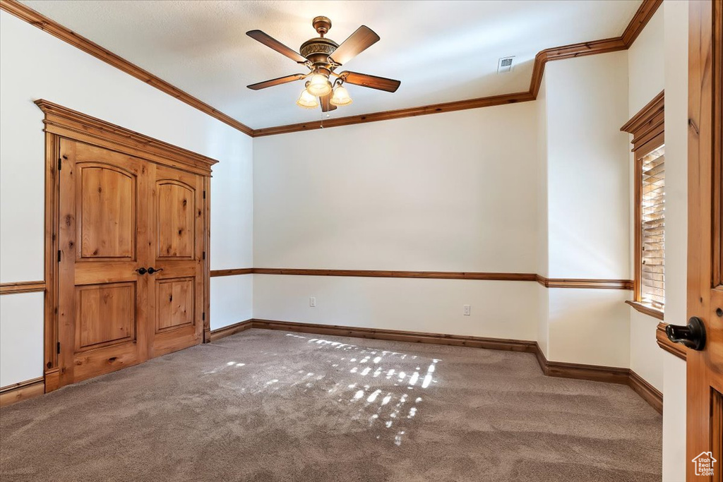 Unfurnished bedroom with dark carpet, crown molding, and ceiling fan