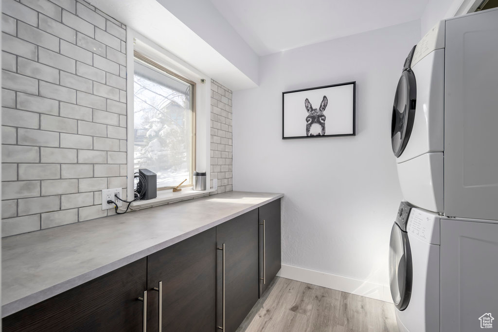 Washroom featuring stacked washer and dryer, light hardwood / wood-style flooring, and cabinets