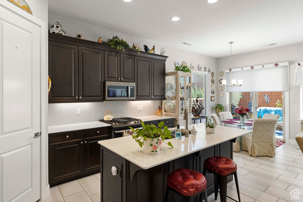 Kitchen featuring a notable chandelier, decorative light fixtures, backsplash, a breakfast bar, and stainless steel appliances