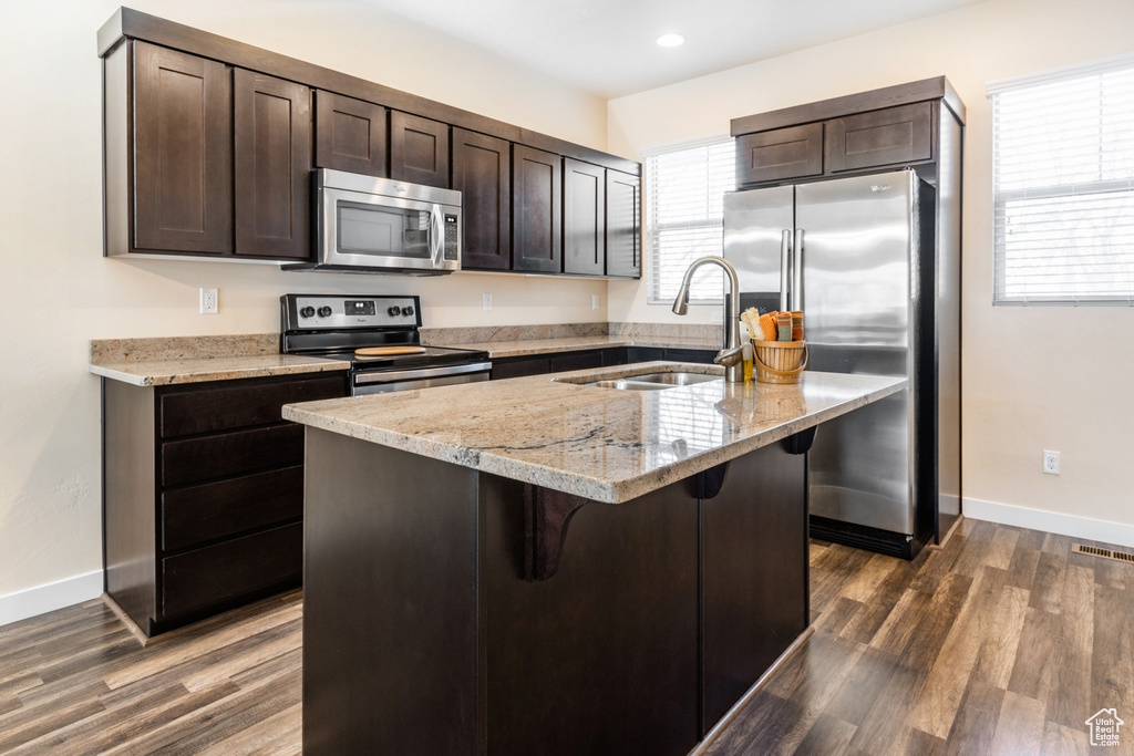 Kitchen with sink, an island with sink, dark hardwood / wood-style floors, appliances with stainless steel finishes, and a breakfast bar