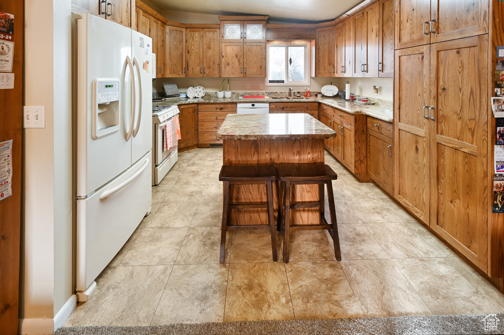 Kitchen with light tile flooring, white appliances, sink, a center island, and a kitchen bar