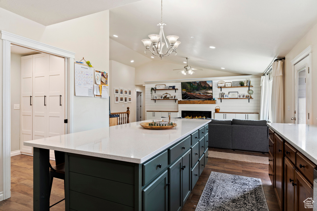Kitchen featuring ceiling fan with notable chandelier, a center island, vaulted ceiling, hanging light fixtures, and dark hardwood / wood-style flooring