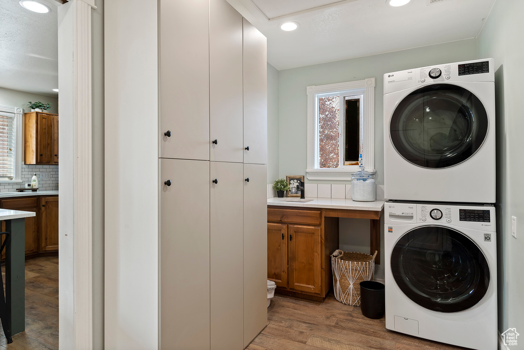 Laundry area featuring stacked washer / drying machine, cabinets, light wood-type flooring, and sink