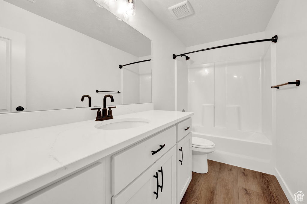Full bathroom featuring wood-type flooring, oversized vanity, shower / bathing tub combination, and toilet