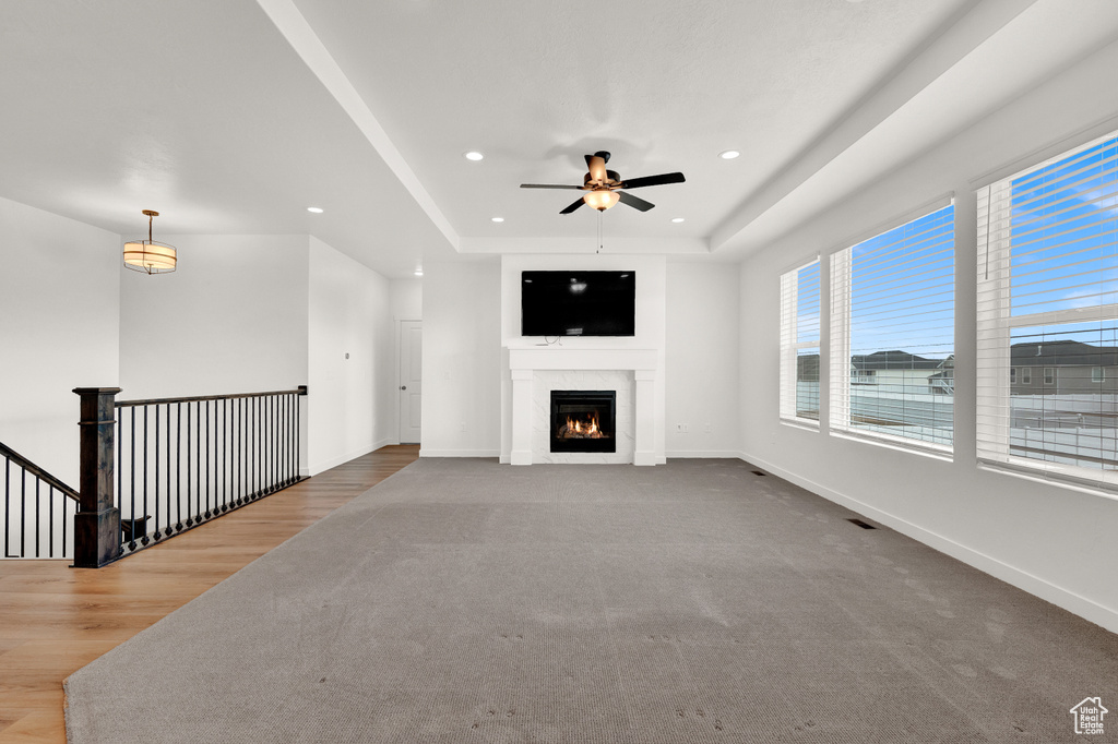 Unfurnished living room with a tray ceiling, light carpet, and ceiling fan