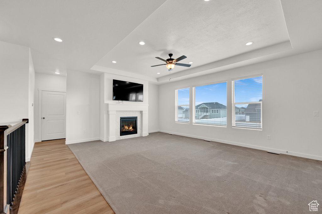 Unfurnished living room with a raised ceiling, light hardwood / wood-style floors, and ceiling fan