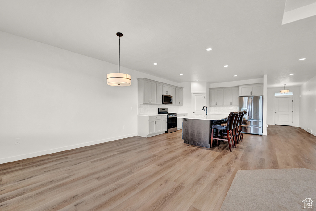 Kitchen featuring appliances with stainless steel finishes, a center island with sink, a kitchen breakfast bar, hanging light fixtures, and light hardwood / wood-style flooring