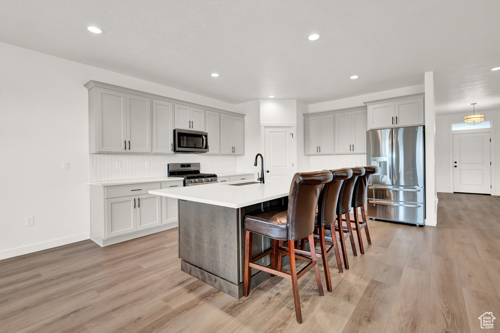 Kitchen featuring sink, a kitchen island with sink, appliances with stainless steel finishes, light wood-type flooring, and a kitchen breakfast bar