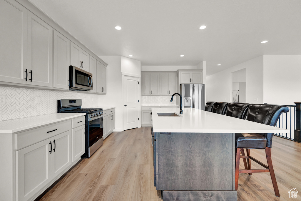 Kitchen featuring a kitchen island with sink, sink, light hardwood / wood-style floors, a kitchen bar, and appliances with stainless steel finishes