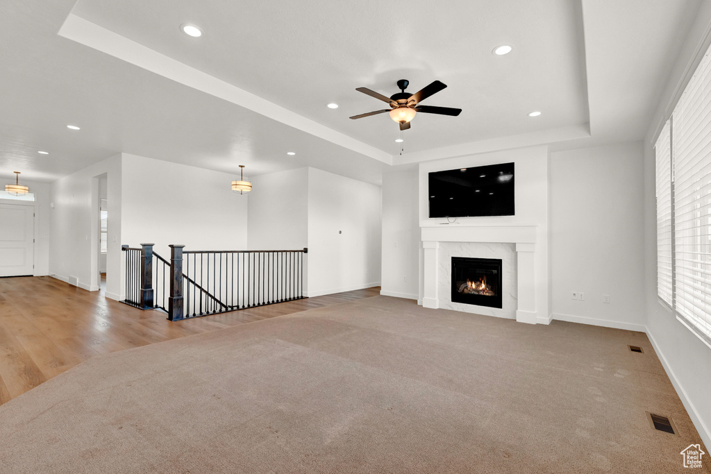 Unfurnished living room with a fireplace, a tray ceiling, light carpet, and ceiling fan