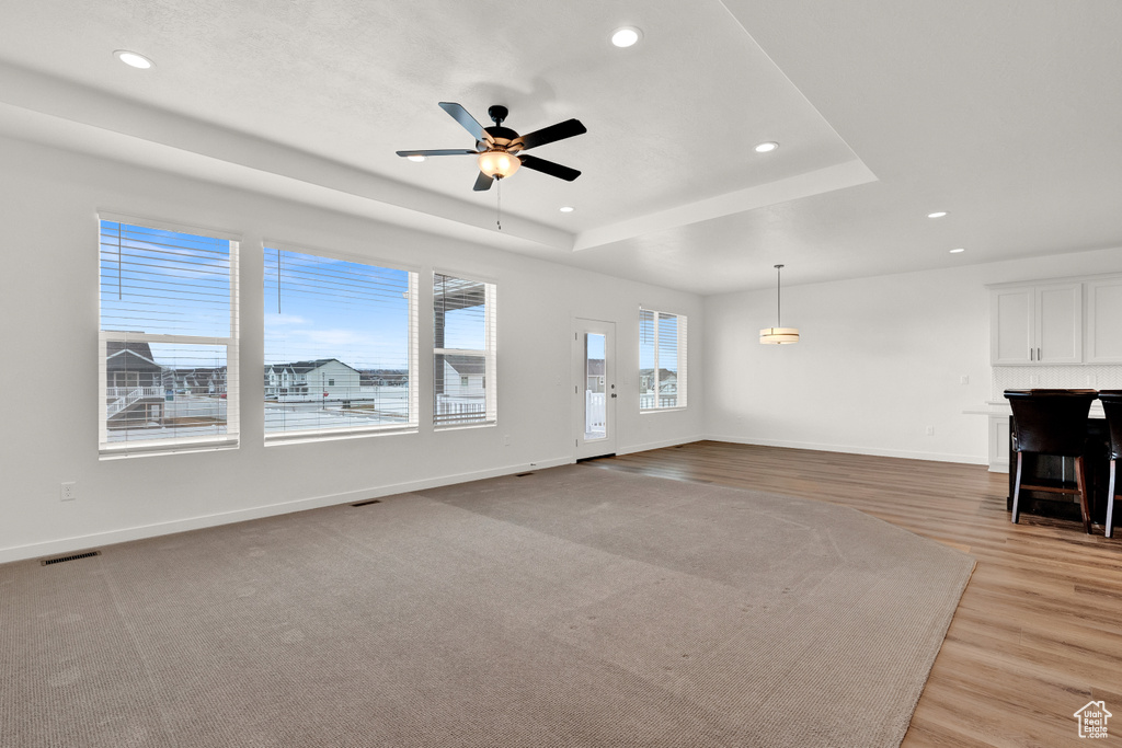 Unfurnished living room featuring a raised ceiling, light hardwood / wood-style flooring, and ceiling fan