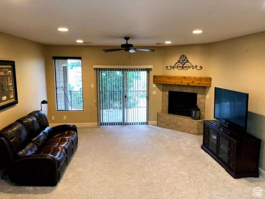 Living room with a fireplace, light colored carpet, and ceiling fan