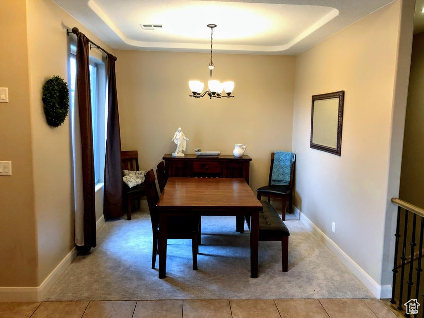 Dining space featuring an inviting chandelier, a tray ceiling, and light tile flooring