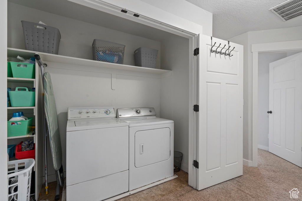 Laundry room featuring washer and clothes dryer, light carpet, and a textured ceiling