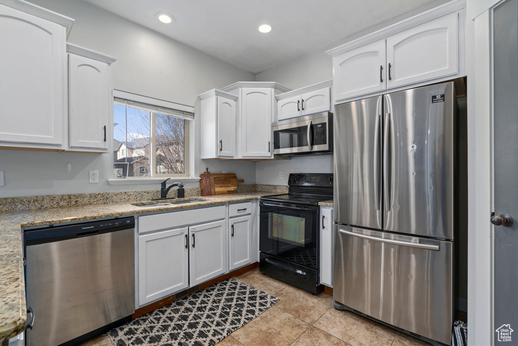 Kitchen featuring sink, appliances with stainless steel finishes, light stone counters, light tile floors, and white cabinets