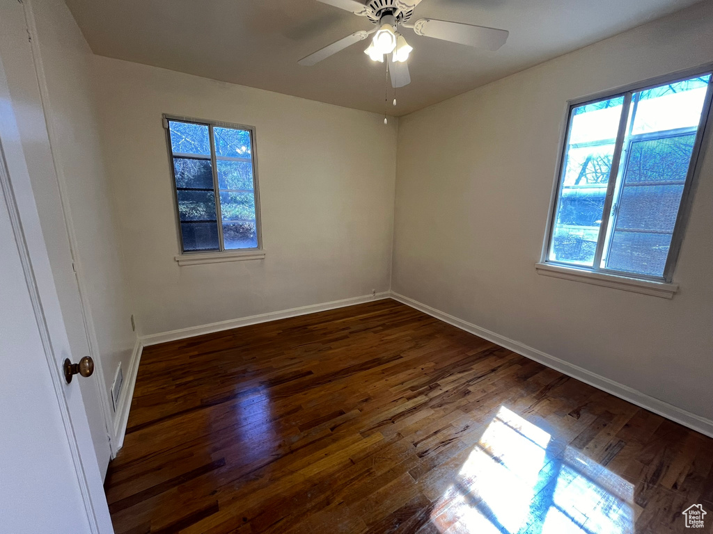 Spare room featuring dark wood-type flooring, ceiling fan, and a healthy amount of sunlight
