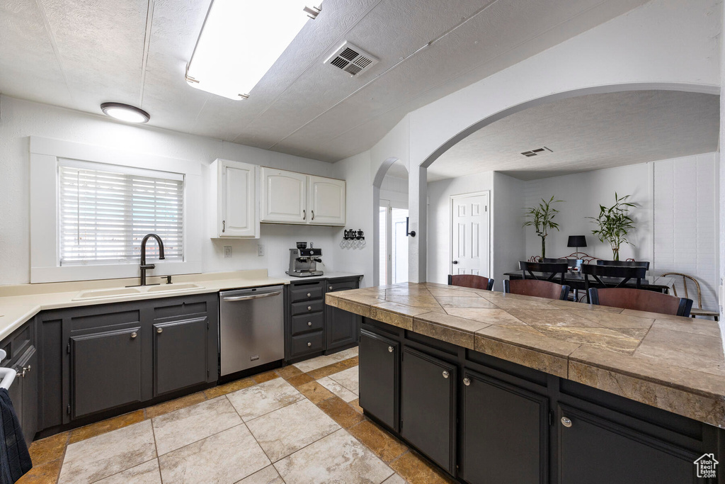 Kitchen featuring a textured ceiling, white cabinets, light tile floors, dishwasher, and sink