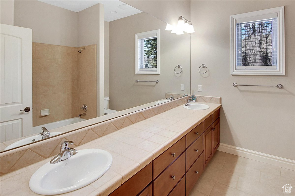 Full bathroom featuring large vanity, tile floors, toilet, double sink, and tiled shower / bath combo