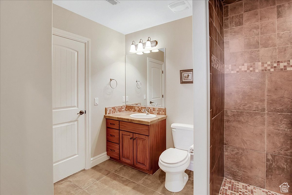 Bathroom featuring tiled shower, vanity, toilet, and tile flooring